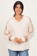 woman wearing a cream-colored long sleeve top with color-blocked sleeves and a v-neckline, smiling at the camera