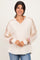 woman wearing a cream-colored long sleeve top with color-blocked sleeves and a v-neckline, smiling at the camera