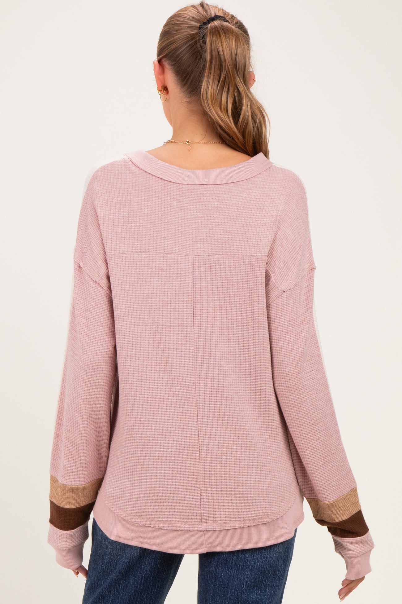 woman wearing a light pink maternity sweater with long sleeves and color block details on the cuffs, styled casually