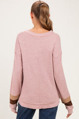 woman wearing a light pink maternity sweater with long sleeves and color block details on the cuffs, styled casually
