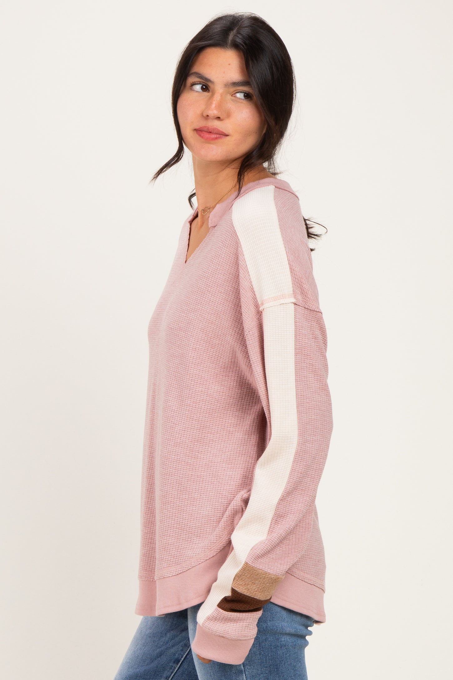 woman wearing a pink v-neck long sleeve top with color block stripes on the sleeves and relaxed fit