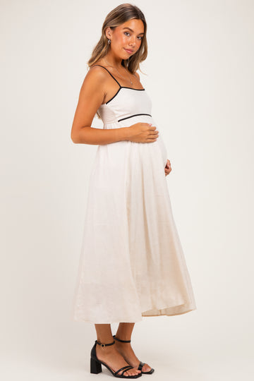 woman wearing a beige maternity maxi dress with black straps and holding her baby bump