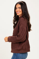 woman wearing a brown cable knit sweater with a mock neckline and smiling against a neutral background