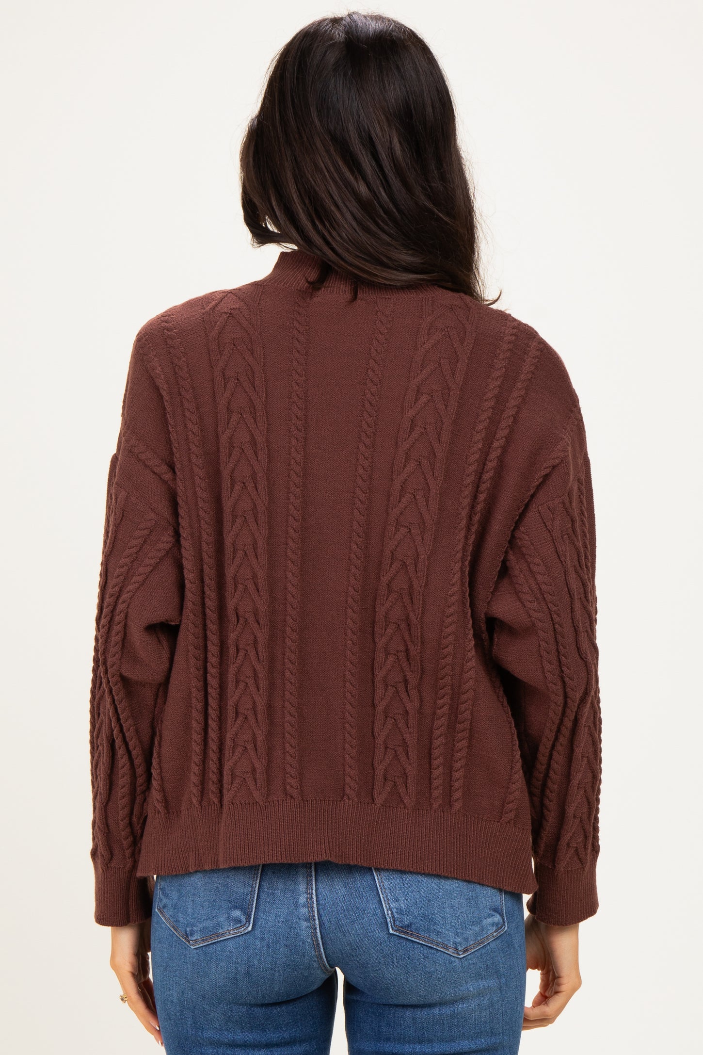 woman wearing a brown cable knit sweater with a relaxed fit and open back, paired with blue jeans