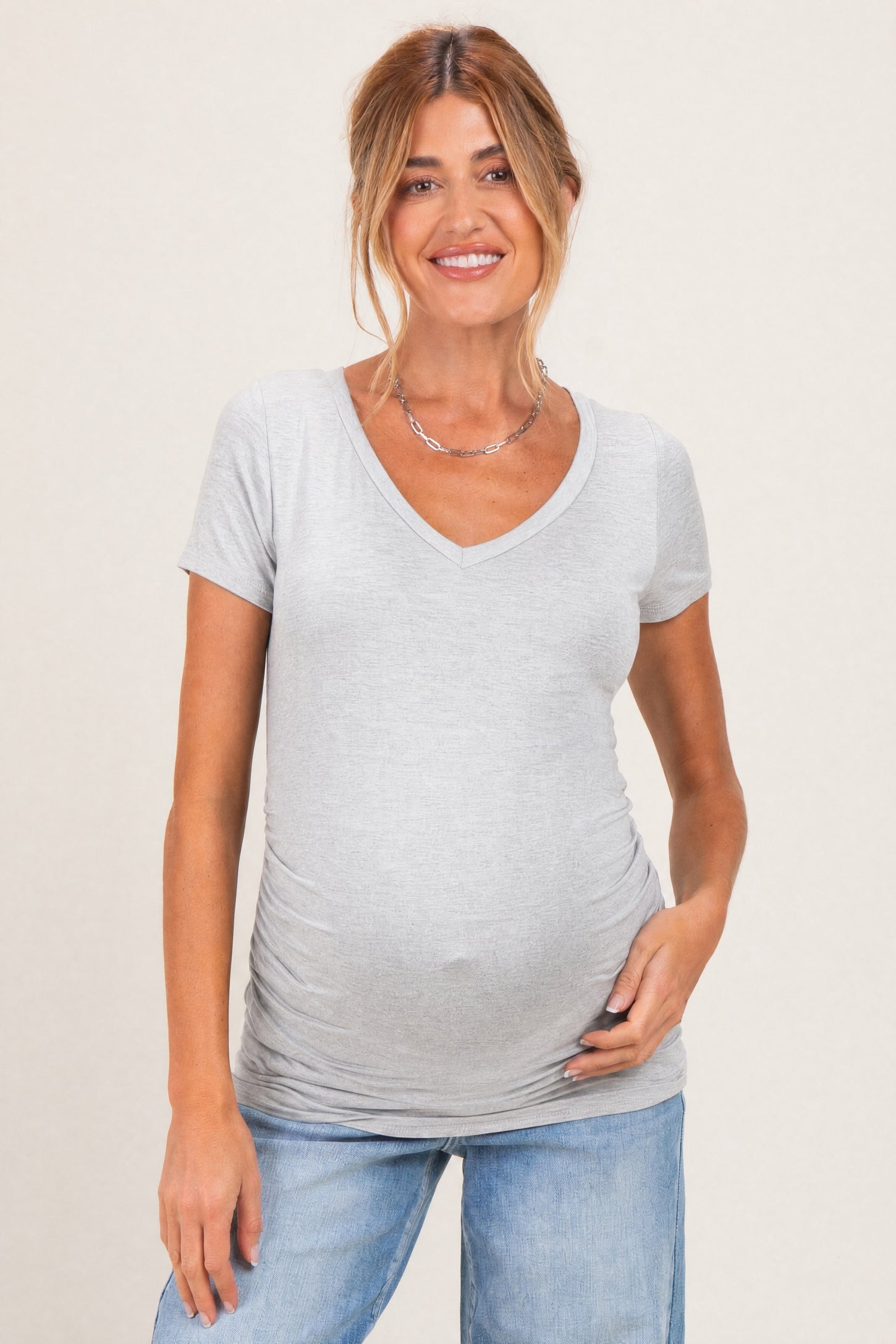 woman wearing a light gray short sleeve maternity top with a v-neck and a visible baby bump
