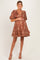 woman wearing a brown floral maternity dress with a v-neck and puff sleeves, gently holding her baby bump