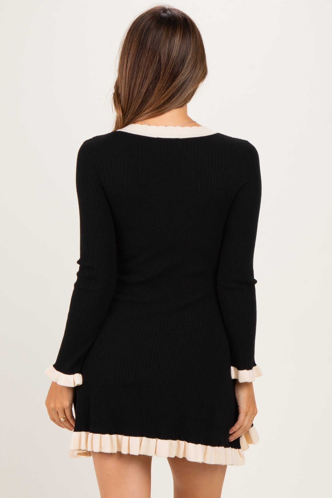 woman wearing a black ribbed maternity dress with cream ruffle details on the sleeves and hem
