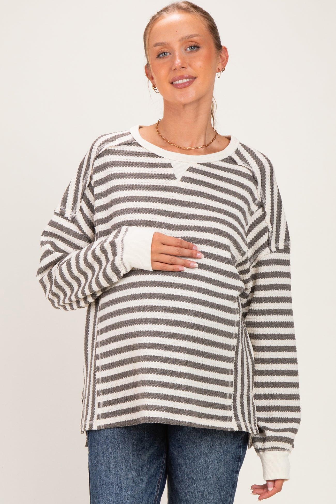 woman wearing a grey and white striped maternity sweater and holding her baby bump