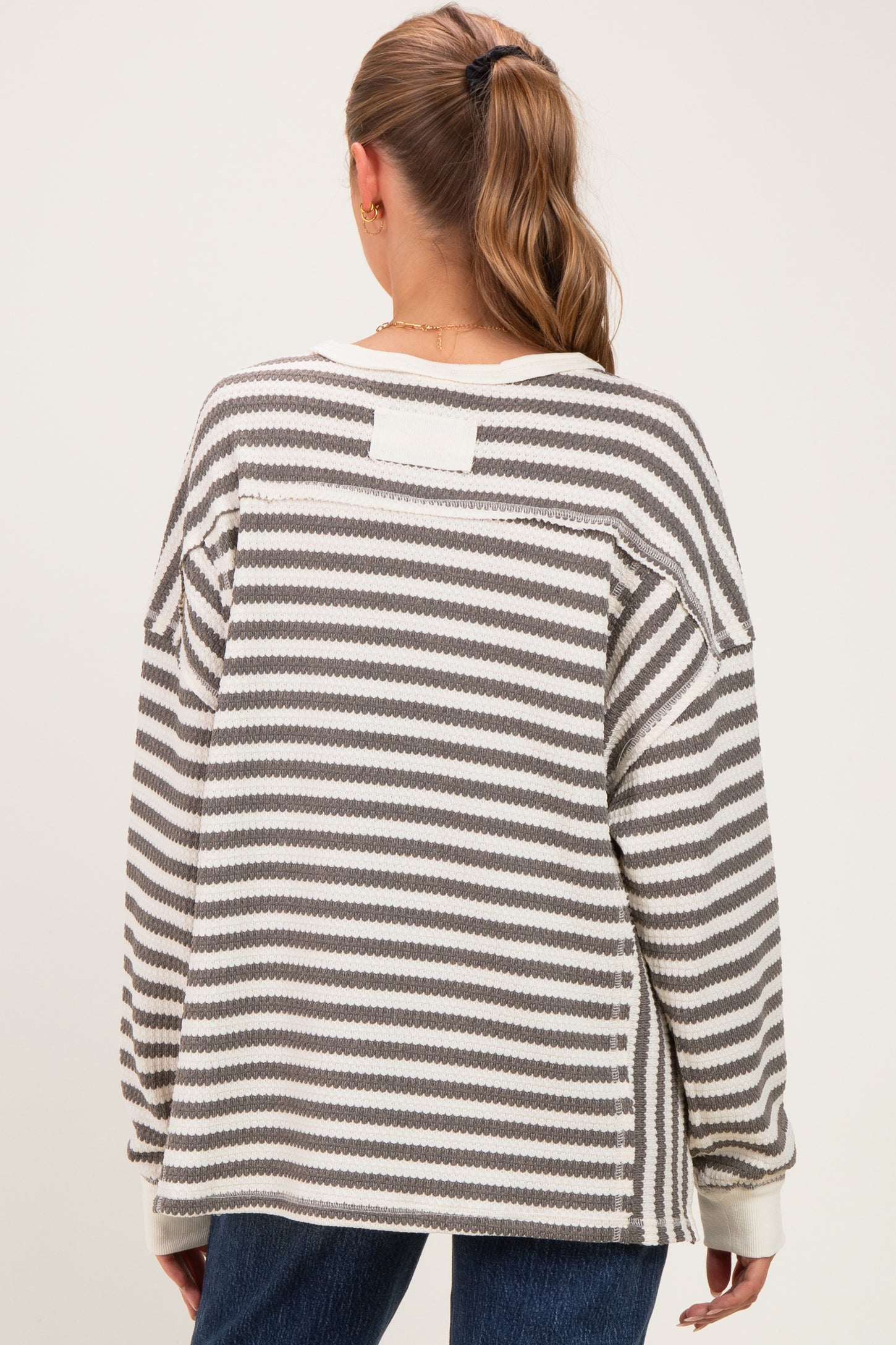 woman wearing a striped maternity sweater in cream and grey with a relaxed fit and wide sleeves, seen from the back