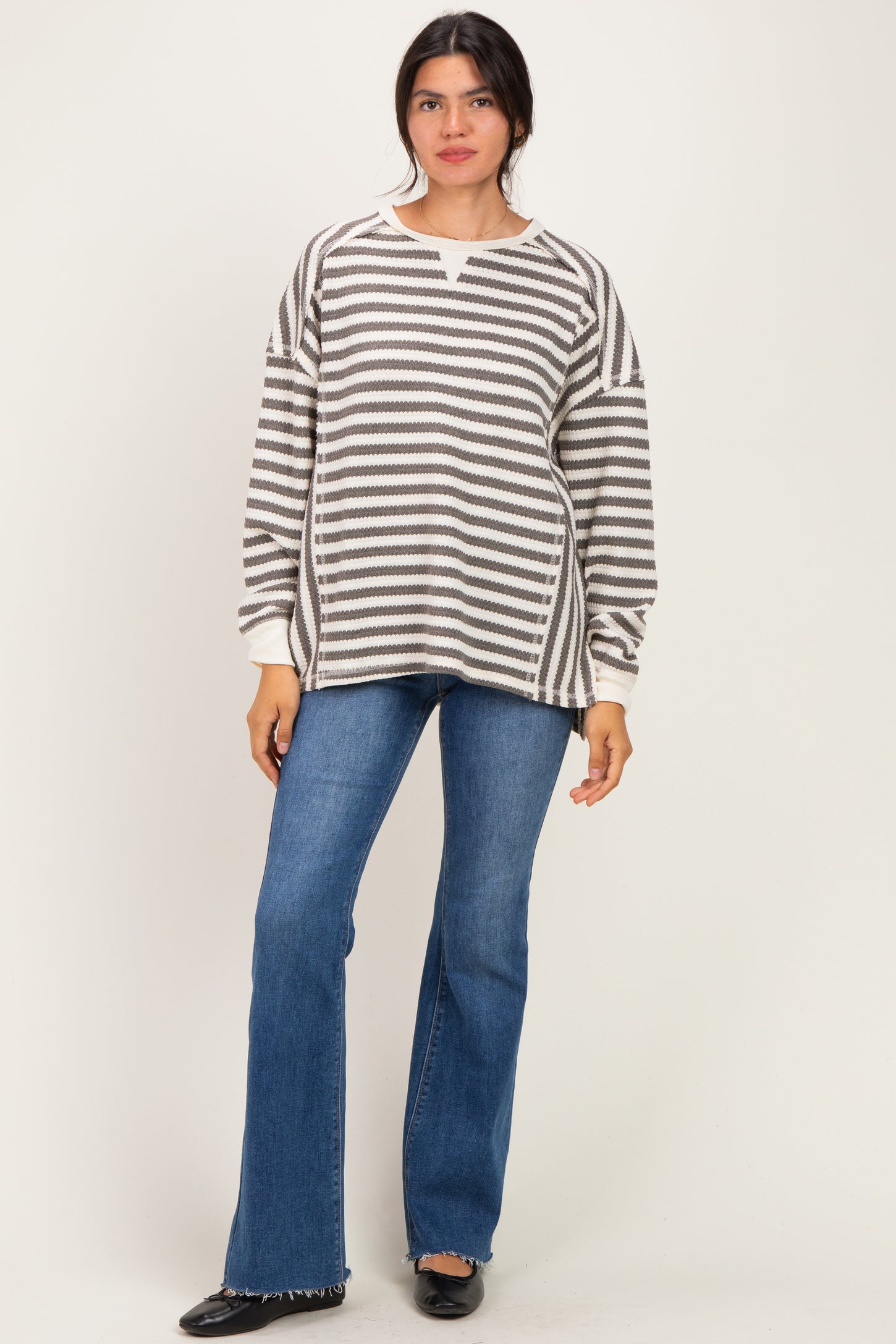 woman wearing a striped oversized sweater with a v-neck and long sleeves paired with flared blue jeans