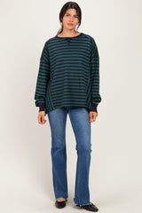 woman wearing a navy and green striped oversized sweatshirt with a crew neck and long sleeves, paired with flared jeans
