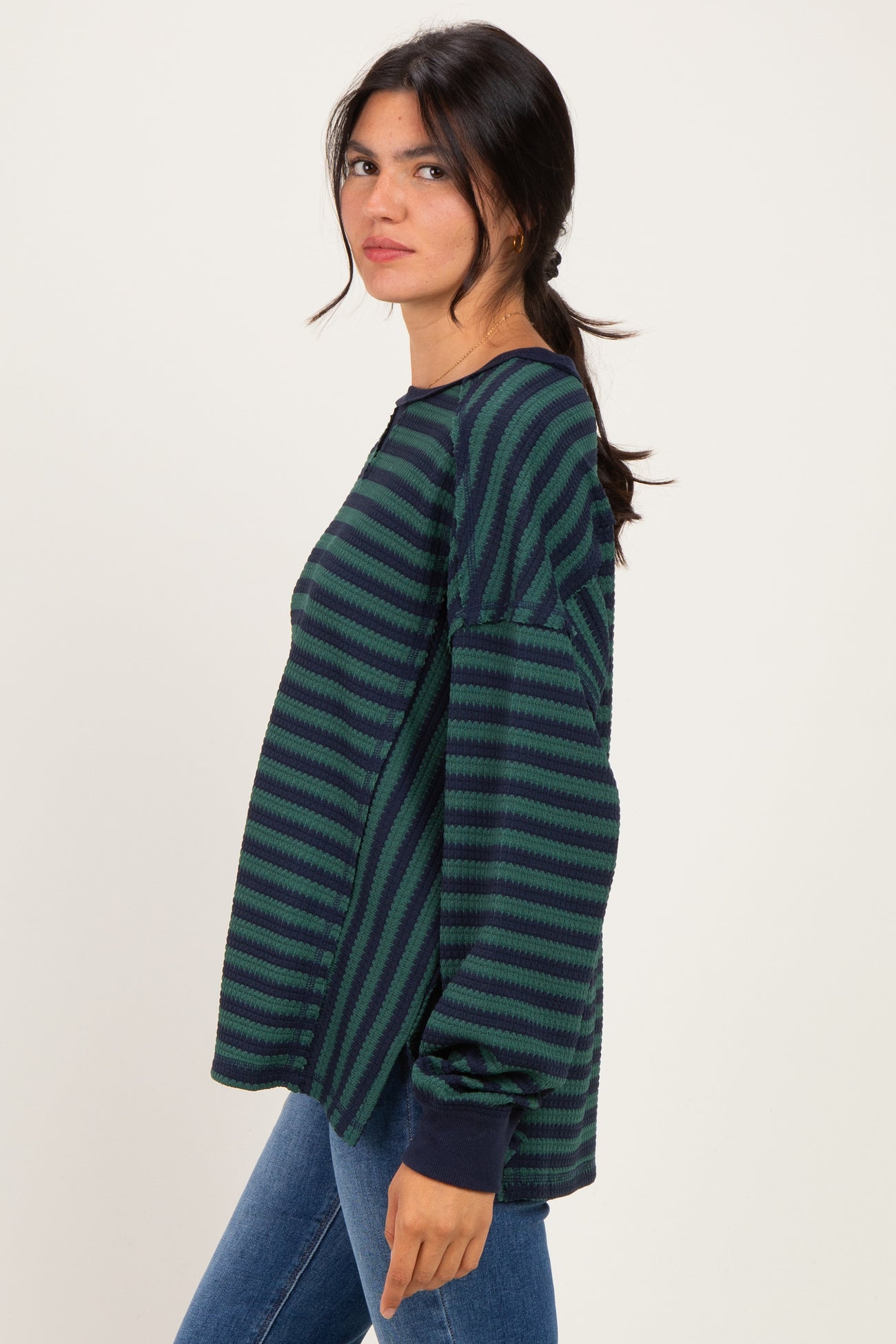 woman wearing a green and navy striped long sleeve top with relaxed fit and side slits, styled with blue jeans