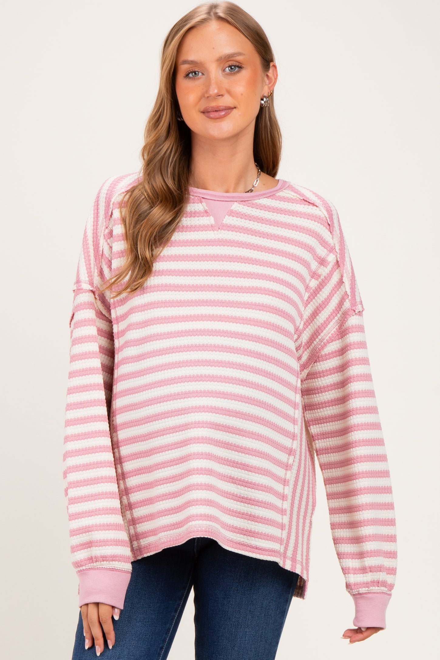 woman wearing a pink and white striped maternity sweatshirt with a relaxed fit and long sleeves, featuring a visible baby bump