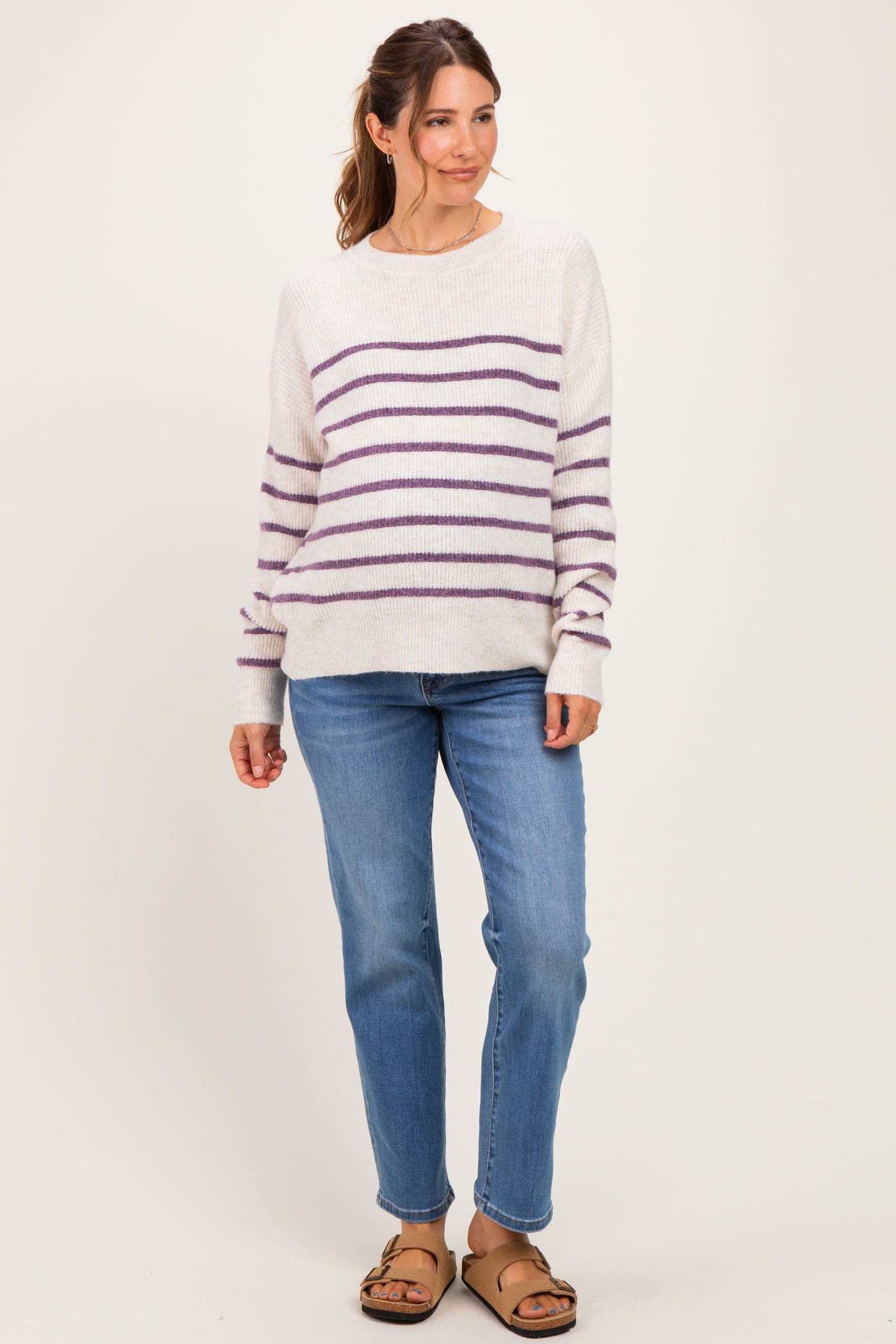 woman wearing a cream striped maternity sweater with purple lines and blue jeans
