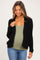 woman wearing a black chunky knit maternity cardigan over a green tank top and showing her baby bump, paired with blue jeans