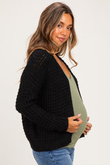 woman wearing a black knit maternity cardigan over a green top, showing her baby bump