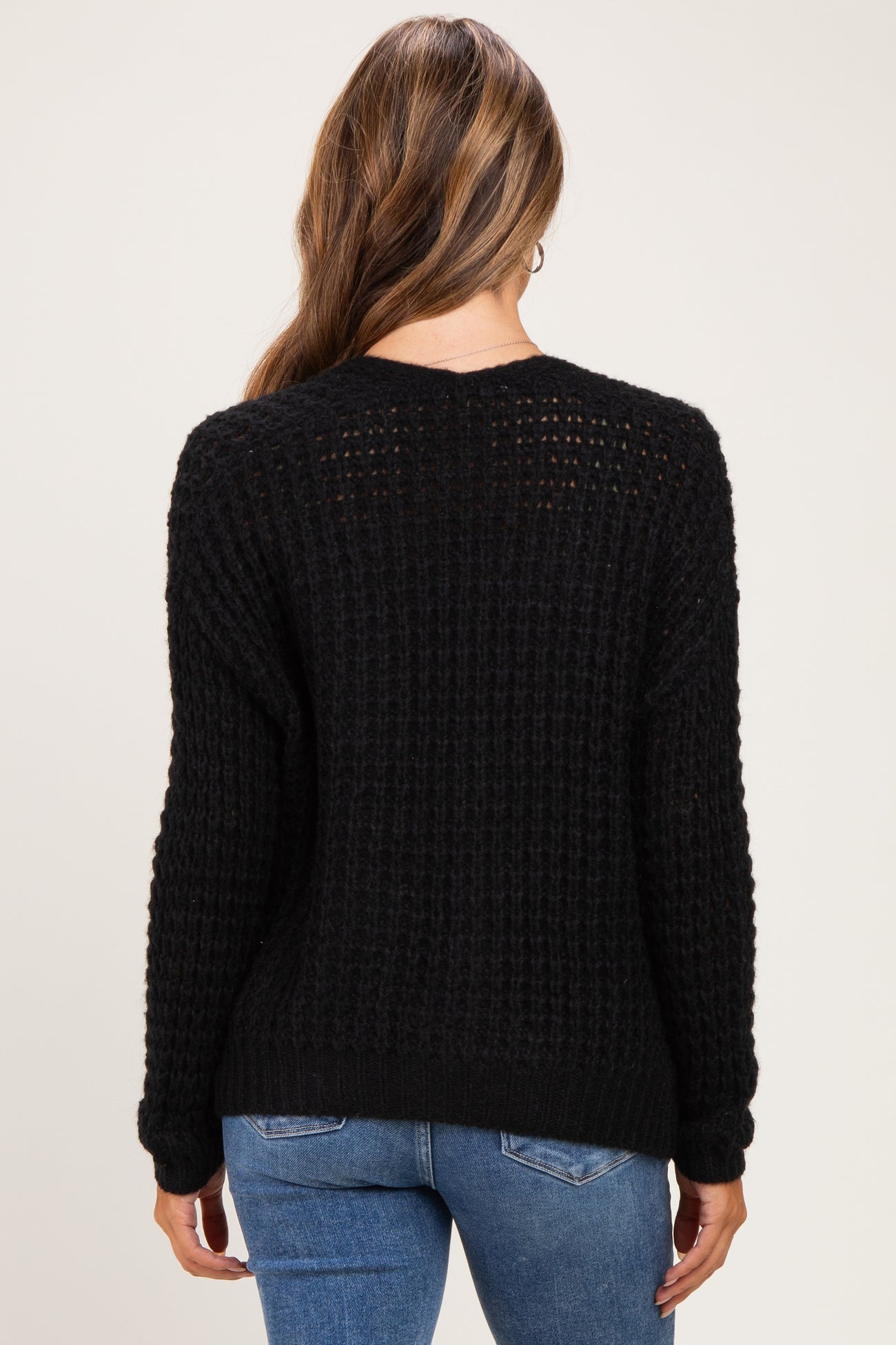 woman wearing a black waffle knit maternity sweater viewed from the back, paired with blue jeans