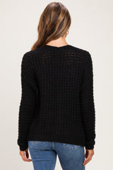 woman wearing a black waffle knit maternity sweater viewed from the back, paired with blue jeans