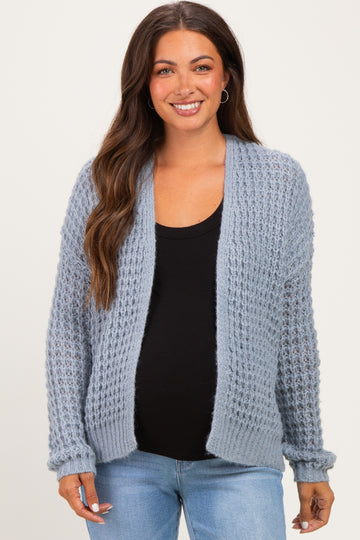 woman wearing a light blue maternity cardigan over a black top, showing her baby bump with a relaxed smile