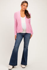 woman wearing a light pink open knit maternity cardigan over a white top and flare jeans with a visible baby bump