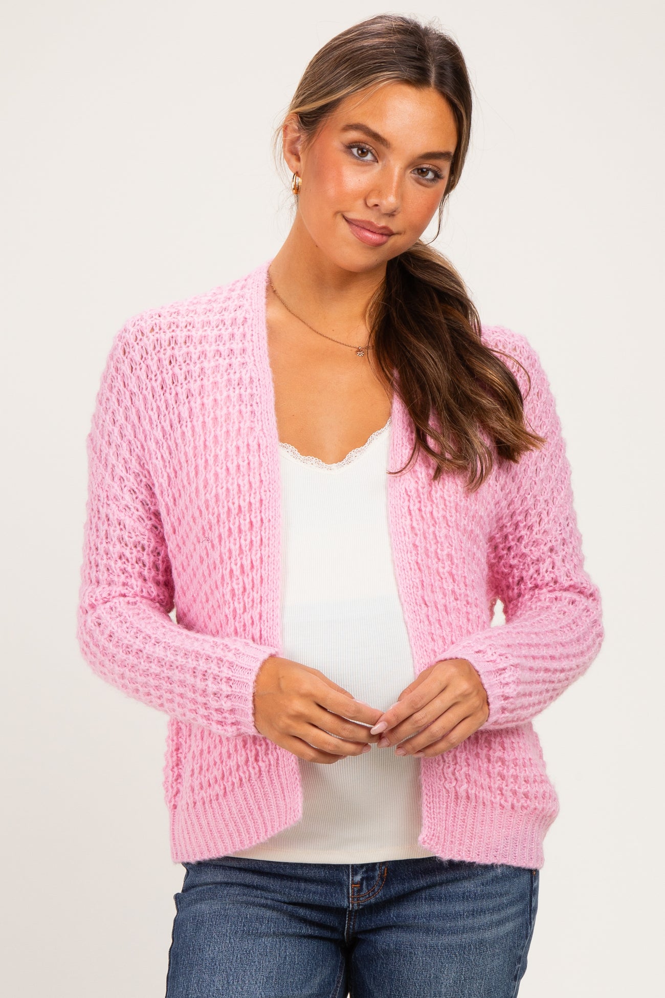 woman wearing a pink textured maternity cardigan over a white top and showing her baby bump