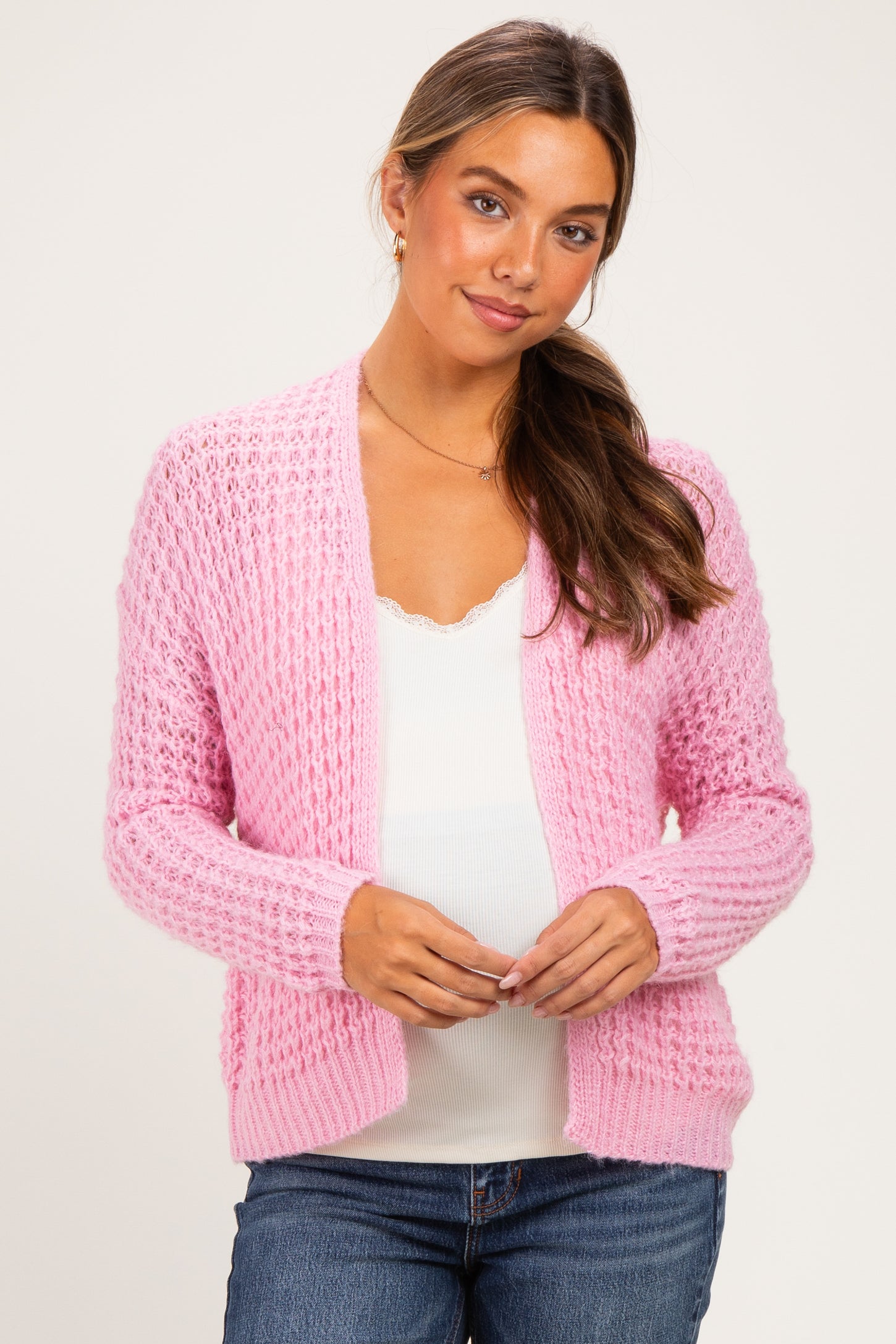 woman wearing a pink textured maternity cardigan over a white top and showing her baby bump