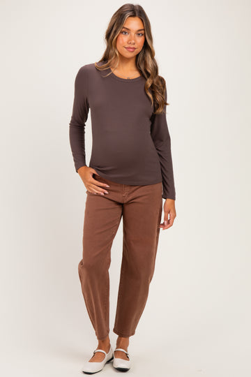 woman wearing a dark brown long sleeve maternity top and brown pants, showcasing her baby bump