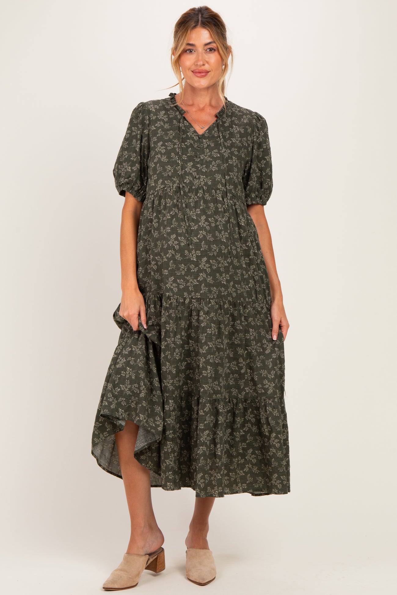 woman wearing a dark green floral maternity dress with short puff sleeves and tiered skirt, showcasing her baby bump