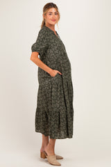 woman wearing a green floral print maternity dress with short sleeves and pockets, showing a baby bump