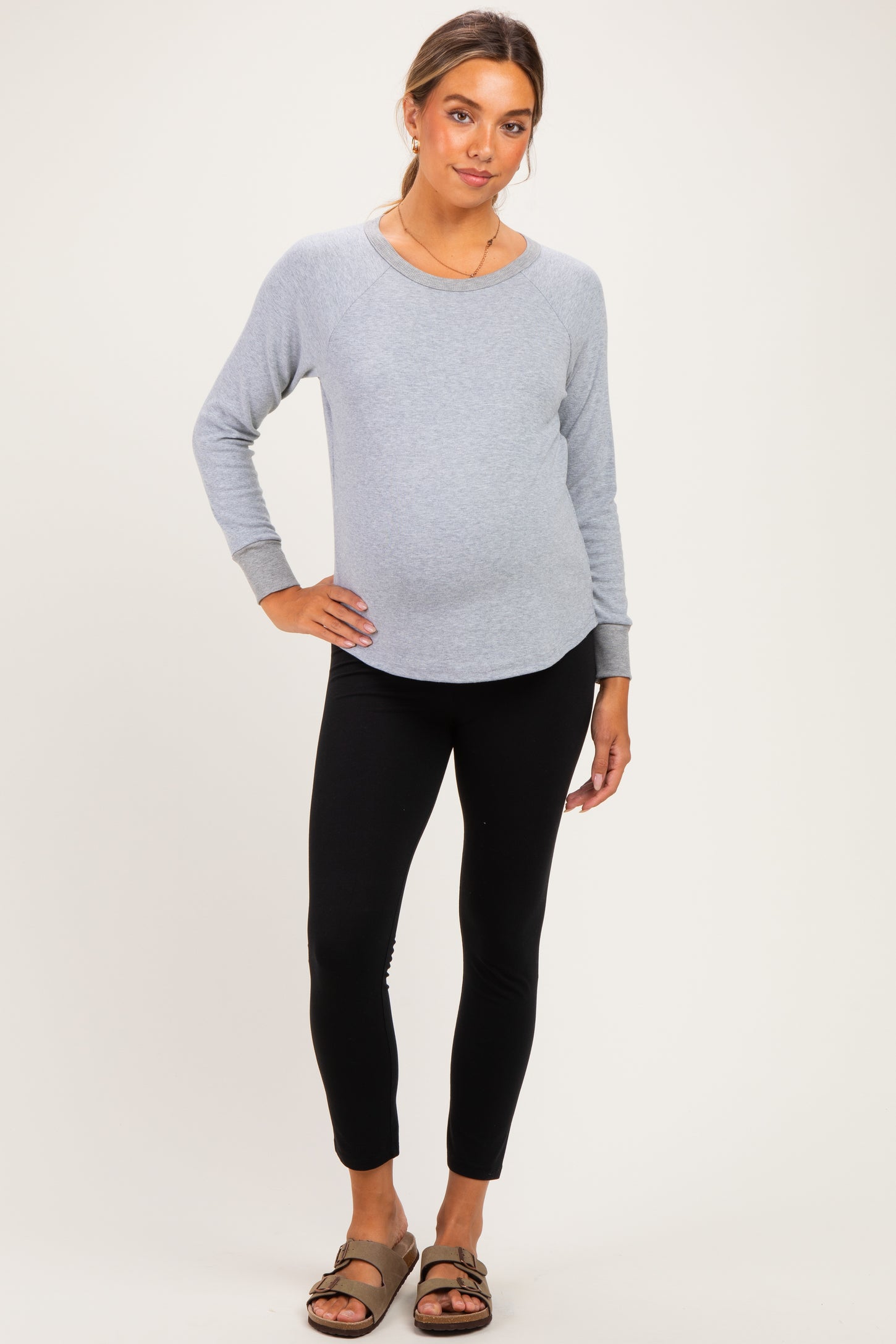 woman wearing a light gray maternity sweatshirt with black leggings and a visible baby bump