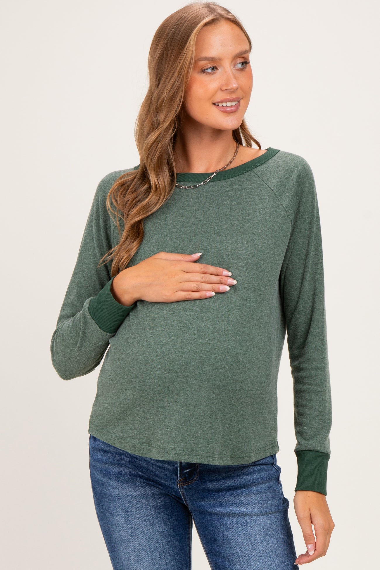 woman wearing a green maternity long sleeve top and holding her baby bump