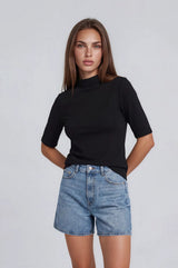 woman wearing a black short sleeve top with a high neck and light blue denim shorts