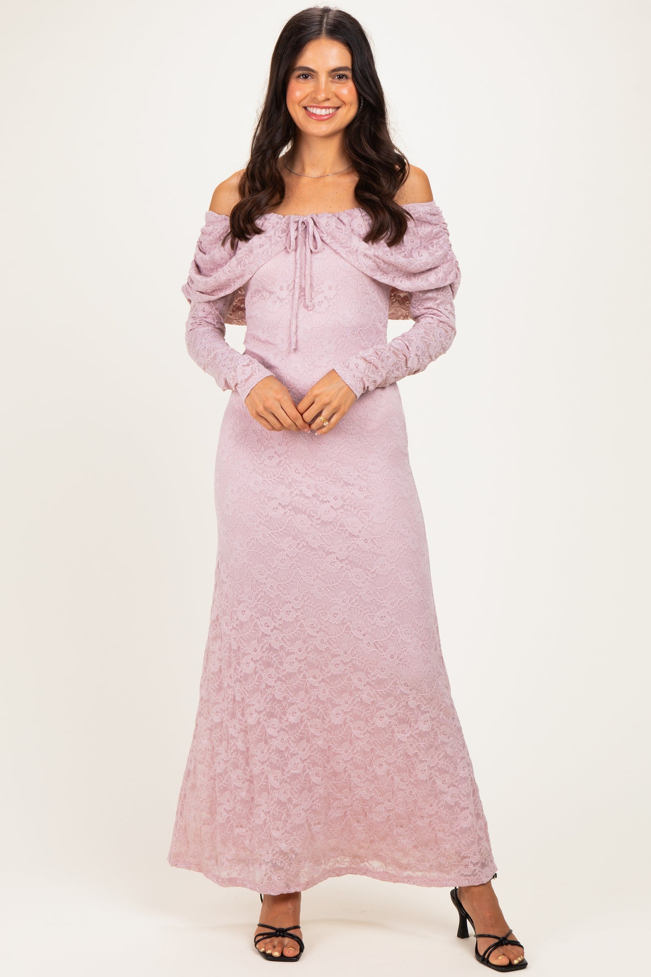 woman wearing a light pink off-the-shoulder lace maxi dress with long sleeves and a tie-front detail
