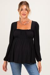 woman wearing a black maternity top with a square neckline and long sleeves, showing her baby bump while smiling