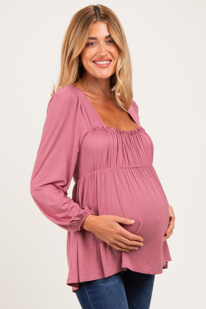 woman wearing a mauve long sleeve maternity top with a gathered neckline and holding her baby bump