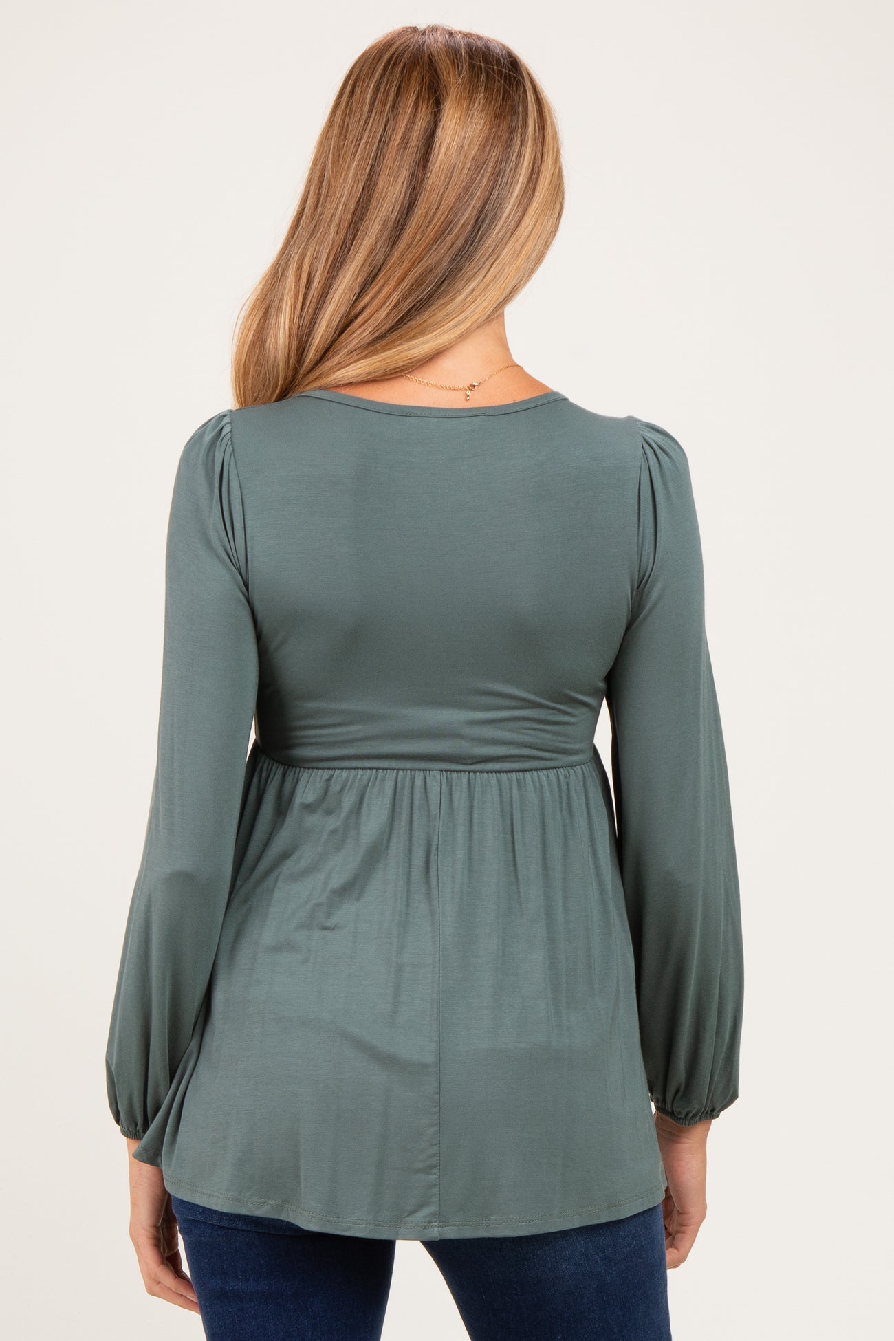 woman wearing a dark green long sleeve maternity top with a fitted bodice and flowing hem