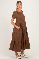 woman wearing a brown tiered maternity dress with short puff sleeves and pockets, showing her baby bump