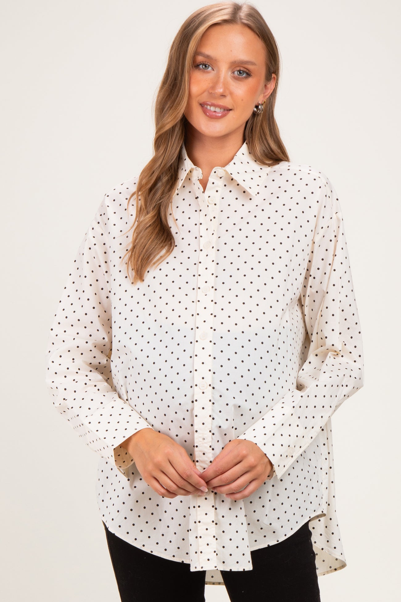 woman wearing a cream maternity shirt with black polka dots and a visible baby bump