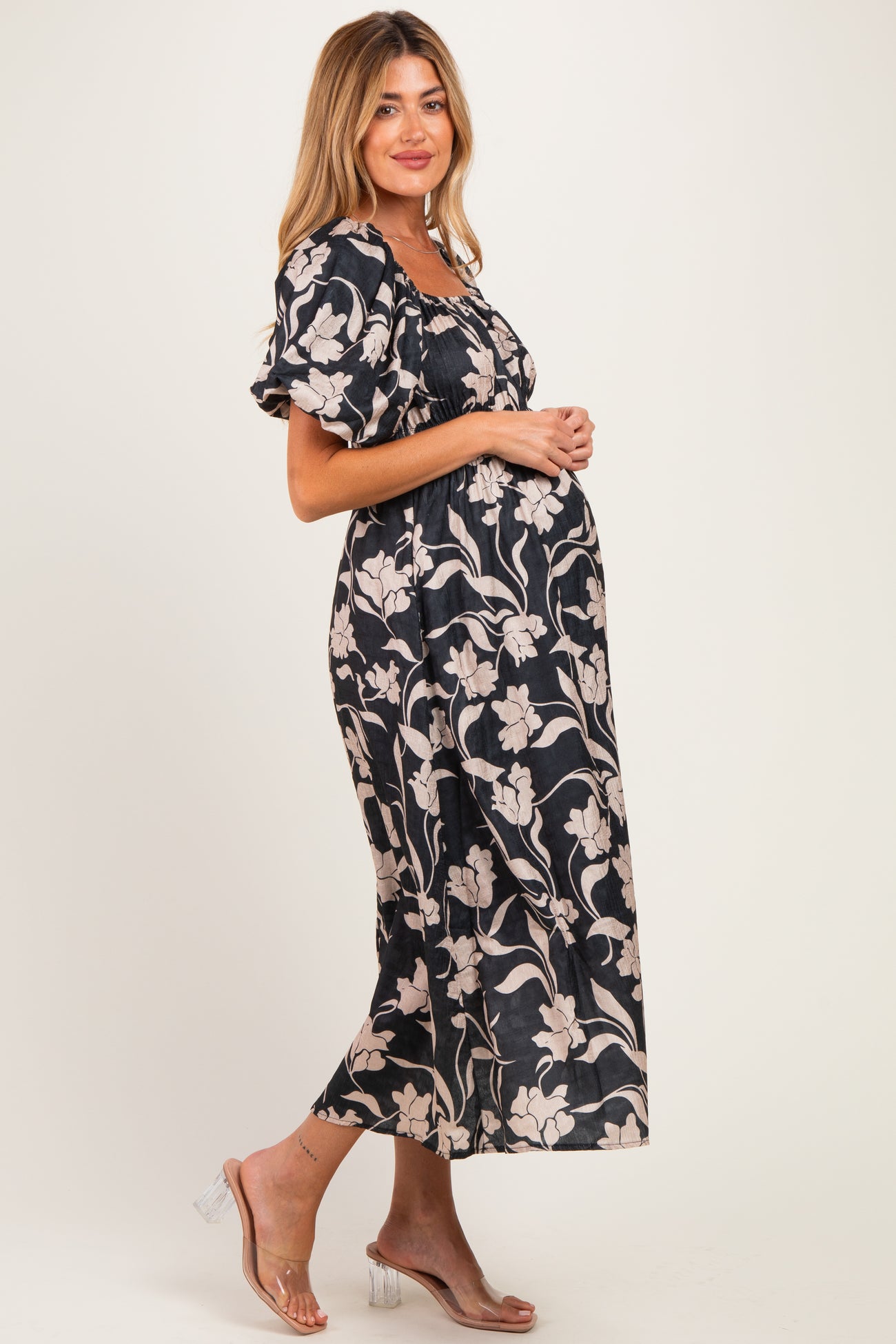 woman wearing a black floral print maternity dress with puff sleeves and a visible baby bump