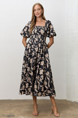 woman wearing a black floral midi dress with puff sleeves and a smocked bodice, standing with hands in pockets