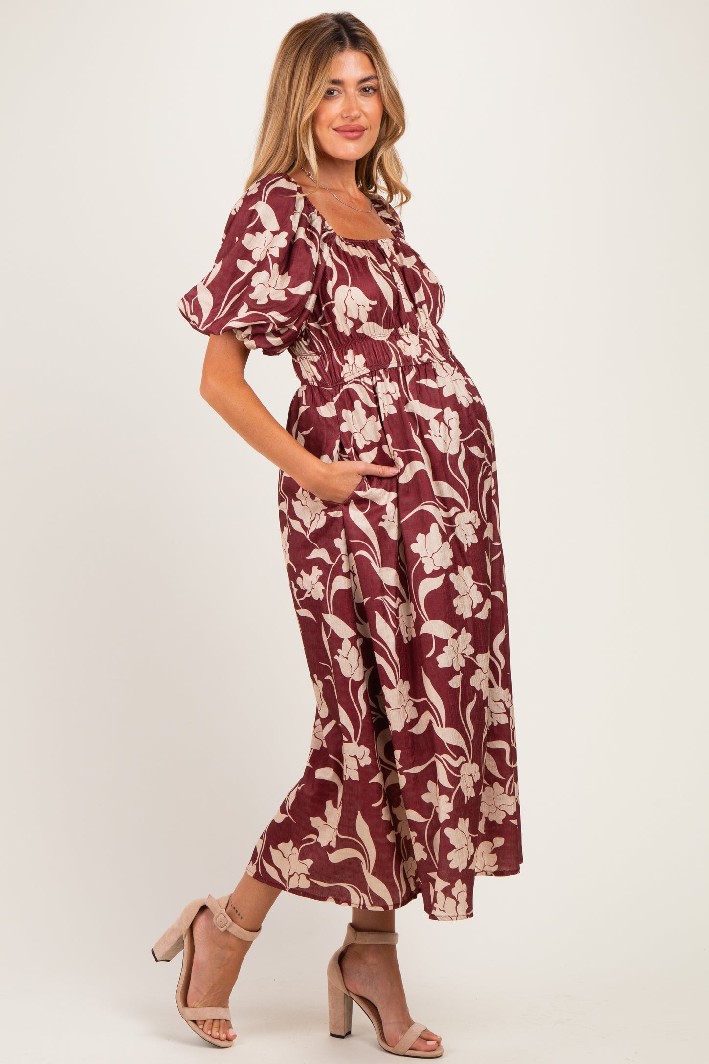 woman wearing a burgundy floral print maternity dress with puff sleeves and side pockets, showcasing a baby bump