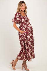 woman wearing a burgundy floral print maternity dress with puff sleeves and side pockets, showcasing a baby bump