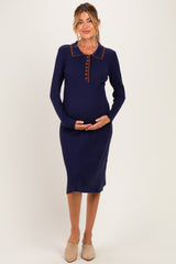woman wearing a navy blue ribbed maternity dress with a collar and button detail, holding her baby bump