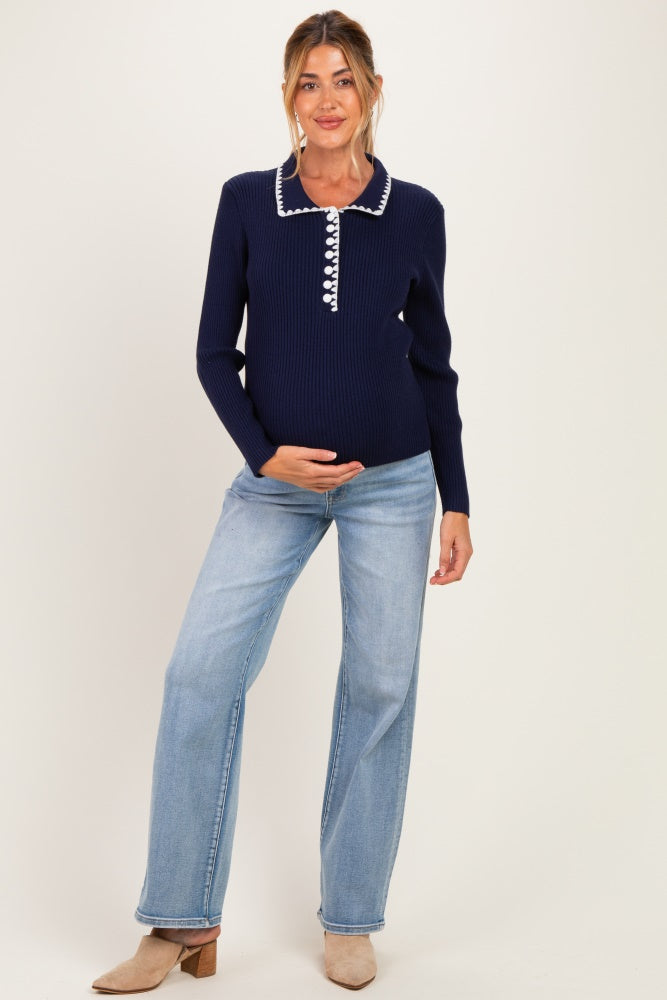 woman wearing a navy blue maternity top with a white collared neckline and stylish buttons, holding her baby bump, paired with light blue jeans