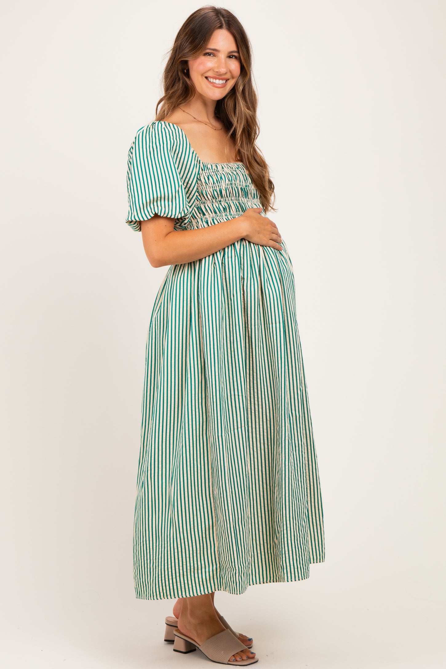 woman wearing a green striped maternity dress with puff sleeves and a fitted bodice, showcasing her baby bump