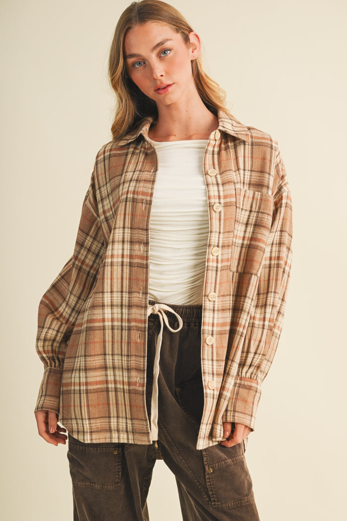 woman wearing a brown plaid oversized shirt over a white fitted top, styled with dark brown pants