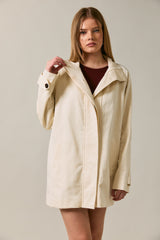woman wearing a cream-colored casual jacket with a collar and front pockets, standing against a neutral background