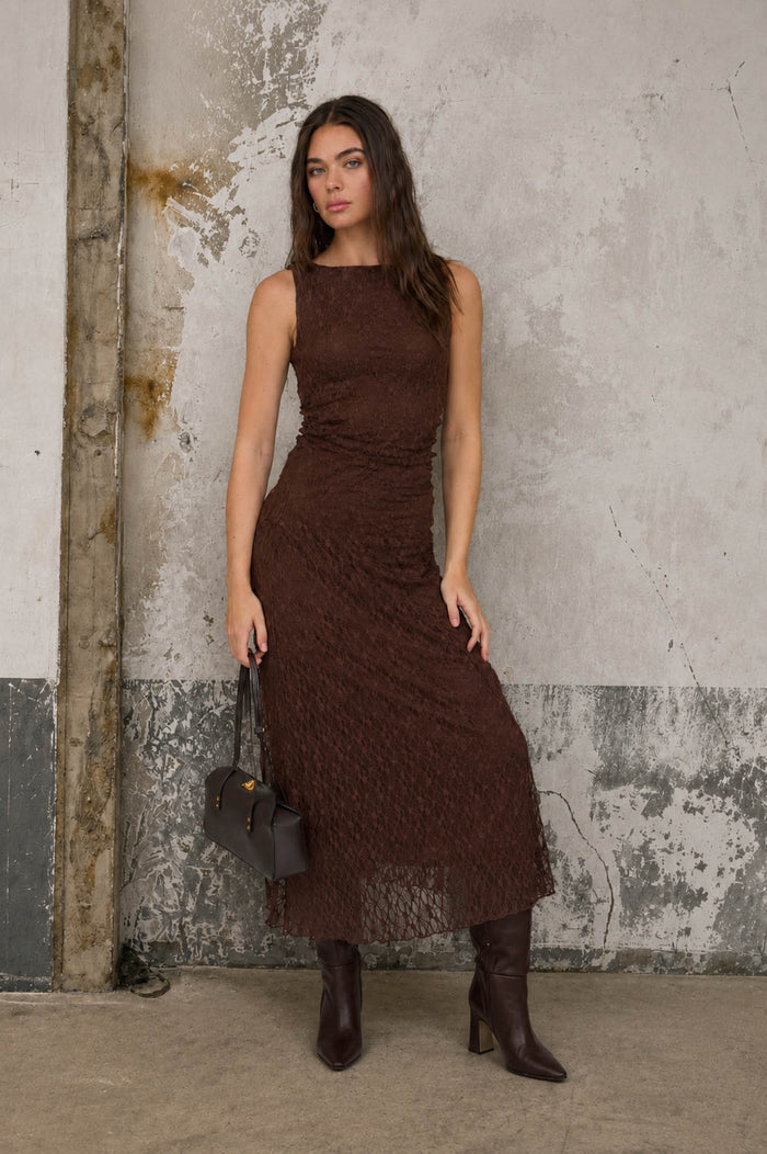 woman wearing a brown lace midi dress with a fitted silhouette and long dark boots, holding a small handbag