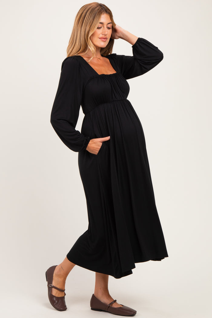 woman wearing a black long sleeve maternity dress with a square neckline and pockets, showcasing her baby bump