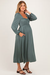 woman wearing a teal long sleeve maternity dress with a square neckline and pockets, showcasing her baby bump